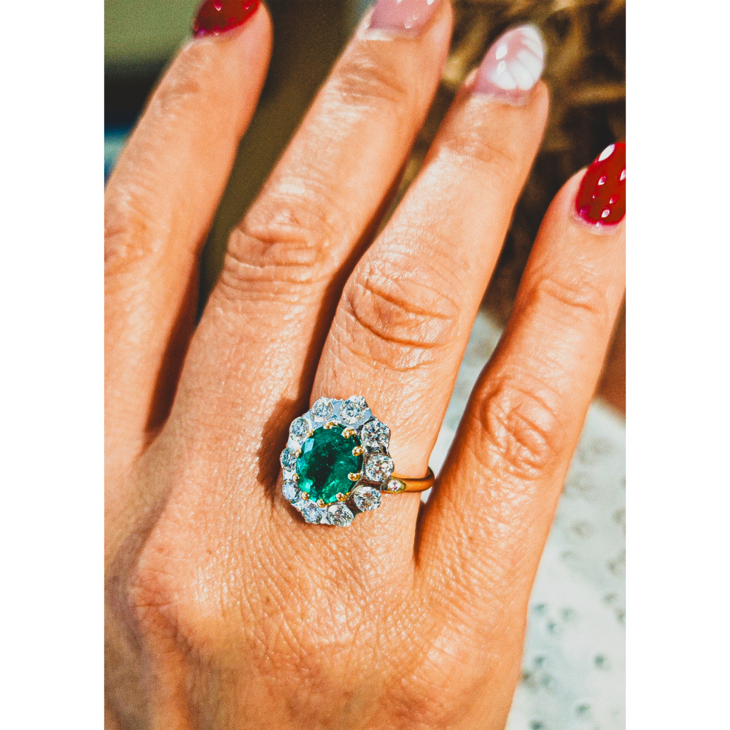 Bague marguerite en or jaune 18 carats sertie d’une émeraude ovale entourée de diamants blancs portée à la main – bijou de luxe femme, bague en or 750 millièmes style joaillerie vintage, bijoux précieux haut de gamme à Paris, bague émeraude et diamants élégante et intemporelle